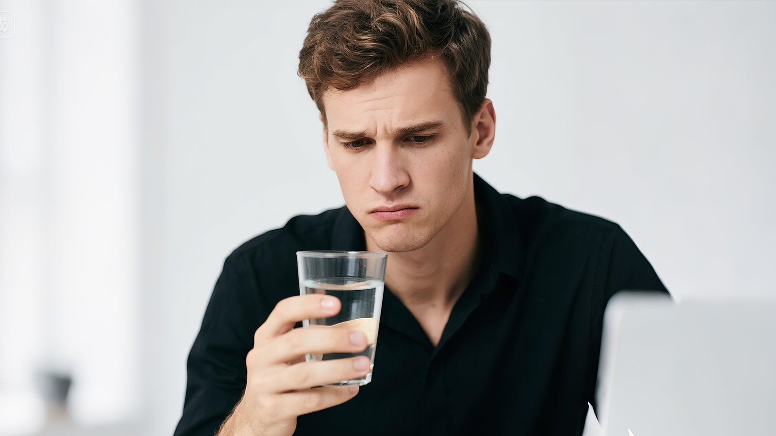 A man looking at a glass of water with a disgusted expression.